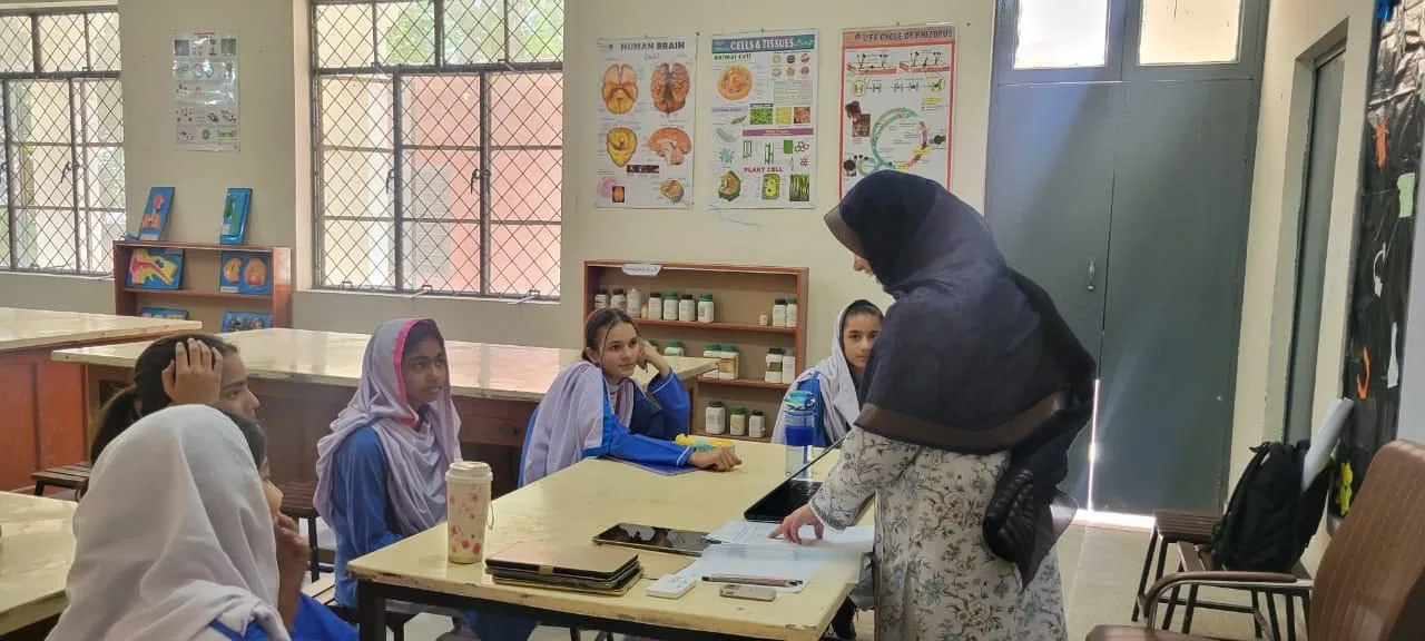 A teacher working with a small group of adolescent girls around a bench in a school science laboratory